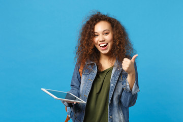 Young african american girl teen student in denim clothes, backpack hold pad pc isolated on blue background studio portrait. Education in high school university college concept. Mock up copy space.