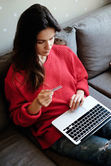 Young woman making online shopping with her laptop sitting on the sofa in the living room