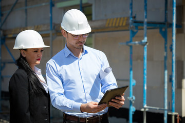 Two architects a man and a woman in construction in white helmets.