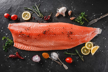 Wall Mural - Fresh raw salmon fish steak with spices on dark stone background. Creative layout made of fish, top view, flat lay.