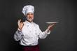 © opolja - Mature cook chef holding an empty plate on a black background.