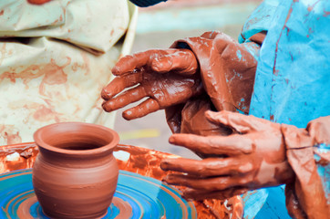 Closeup of children's hands in brown clay sculpting a pot on a potter's wheel with blue background