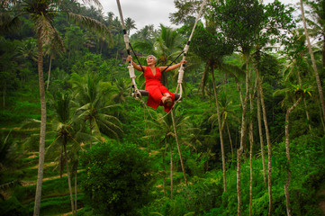 Wall Mural - attractive happy middle aged 40s or 50s Asian Indonesian woman with grey hair riding rainforest swing carefree swinging and enjoying tropical jungle adventure