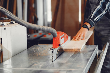 Canvas Print - A man carves a tree. The carpenter works with saw in a studio. An engineer provides a tree shape