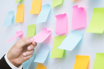 Wall Mural - close up hand people business man post it notes in the wall at meeting room. Sticky note paper reminder schedule board. Colorful variety copy empty space. soft focus.