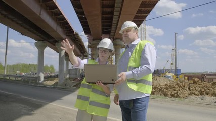 Wall Mural - man and woman working on construction site. manager and architect discuss future installation plan for construction of overpass using laptop.