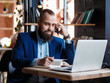 © Ilnur - young bearded businessman at work in the office. A man sits at a laptop talking through a mobile phone. telephone conversations in coworking