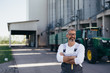 © cherryandbees - worker standing crossed arms, blurred grain silo in background