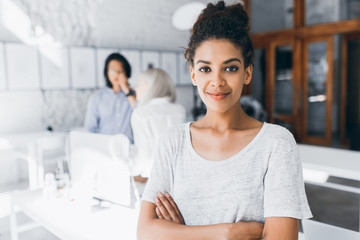 Wall Mural - Portrait of inspired female black office worker wearing white t-shirt. Indoor photo of students of international university preparing for exams with charming african girl on foreground.