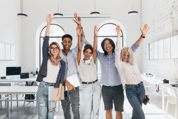 Wall Mural - International tired students celebrating end of exams and laughing in lecture hall. Happy freelance programmers done with long project and posing with smile, holding laptops.