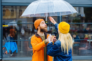 Side view portrait of lovely hipster couple face to face openinig transparent umbrella lsmiling enioying meet in rainy spring cold weather urban city street on background. Lifestyle concept.