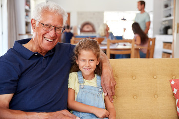 Wall Mural - Portrait Of Grandfather Sitting With Granddaughter On Sofa At Home