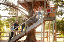 Multi-Generation Family Climbing Outdoor Wooden Platform To Tree House In Garden