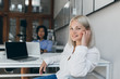 © Look! - Female web-developer posing with smile in office while her asian male colleague working on project. Chinese marketer using laptop sitting at the table with pretty european manager.