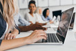 © Look! - Blonde woman with elegant hairstyle typing text on keyboard in office. Indoor portrait of international employees with secretary using laptop on foreground.