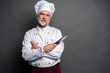 © opolja - Portrait of a mature chef cook holding knifes isolated on a black background.