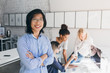 © Look! - Indoor portrait of successful asian it-specialist standing with arms crossed and smiling. African female office worker discussing new project with web-designers while her chinese colleague posing.