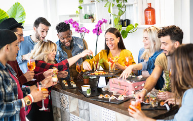 Group of friends having fun at pre dinner party aperitif buffet drinking cocktails and eating snacks - Young people spending time together at home - Bright vivid filter with natural interior lighting