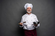 © opolja - Smiling mature male chef with bowl and cooking vane in hands on black background.