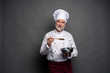 © opolja - Smiling mature male chef with bowl and cooking vane in hands on black background.