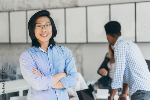 Pleased Asian Student With Long Hair Standing In Confident Pose In