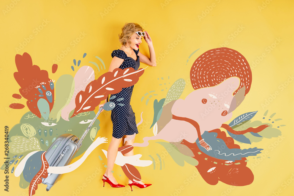 top view of young shocked elegant woman with suitcase lying on yellow background with floral illustration - obrazy, fototapety, plakaty 