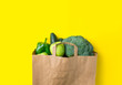 Green raw organic vegetables fruits broccoli cucumbers bell peppers apples in brown paper Kraft grocery bag on yellow background. Healthy diet dietary fiber vegan plastic free concept. Poster banner