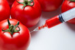 Close-up shot of a syringe injecting a red liquid to fresh red tomatoes. Concept of genetic modification.
