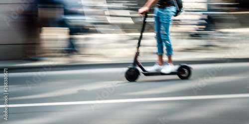 Fotomural Elektroroller fährt auf einer Straße durch die Stadt