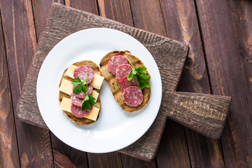 Wall Mural - open sandwiches with salami slices rye bread cheese topped parsley on white plate wooden cutting board top view