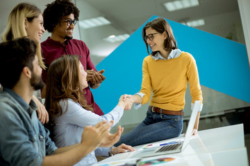 Wall Mural - Group of young coworkers interacting around a table and handshaking in the office