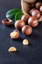 Australian Macadamia Nuts With Green Leaves Spilled Out Of The Bag On Black Scratched Background
