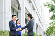 © DragonImages - Asian young businessman smiling and greeting his colleague with assistant outdoors near the office building