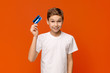 © Prostock-studio - Cute boy holding credit card, orange studio background
