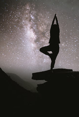 Wall Mural - Colorful night sky with stars and silhouette of a standing girl  yoga on the stone. Blue milky way with girl on the mountain. High Rocks. Background with galaxy and silhouette of a girl.