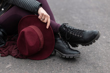 Young Woman With An Elegant Vintage Purple Hat In Pants In Leather Fashionable Black Shoes Is Sitting On The Asphalt. Stylish Women's Headdress And Shoes. Modern Street Style. Close-up.