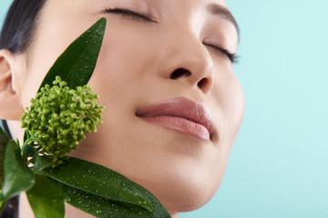 Low angle of attractive Asian lady posing with branch of plant