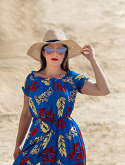 Portrait of a Beautiful Female Standing on a Big Rock Wearing Sunglasses and Touching her Summer Hat