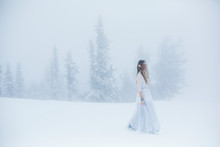 Woman Wearing Elf Ears, Dreadlocks And White Dress In Winter Snowy Christmas Tree Forest. Fog And Mystery Frozen Day
