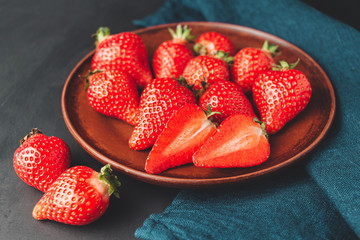 Red strawberry in the plate at dark background with blue napkin