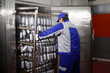 © Alla - A slaughterhouse worker places products in the smokehouse. Shelving with finished products sausages. The worker is standing with his back, his face is not visible. Sausages in the package.