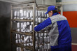 © Alla - A slaughterhouse worker places products in the smokehouse. Shelving with finished products sausages. The worker is standing with his back, his face is not visible. Sausages in the package.