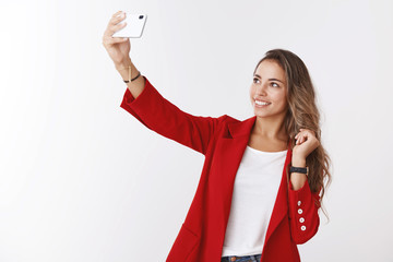 Wall Mural - Girl smiling confident sassy having lucky day feeling upbeat taking selfie sunny spring weather wearing red jacket extending arm holding smartphone upper angle photo grinning device display