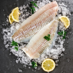 Fresh raw fillet white fish Pangasius with spices on ice over dark stone background.  Seafood, top view, flat lay, copy space