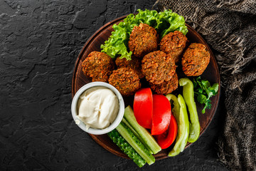 Roasted chickpeas falafel patties with garlic yogurt sauce, served with lettuce and fresh vegetables in a plate over dark stone background. Healthy vegan food, clean eating, dieting, top view