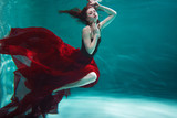 beautiful young woman in a red dress swims under water