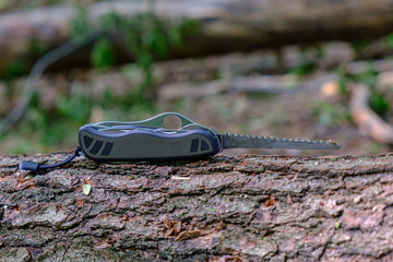 Multitool outdoor equipment, Swiss Soldier's Knife with extended saw blade on tree trunk in forest