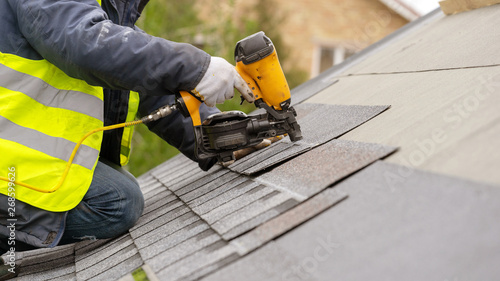 Fotografía Workman using pneumatic nail gun install tile on roof of new house under constru