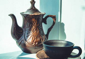 A teapot and a cup of clay are standing near the window.