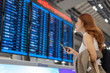 © geargodz - woman using smartphone with flight information board at airport